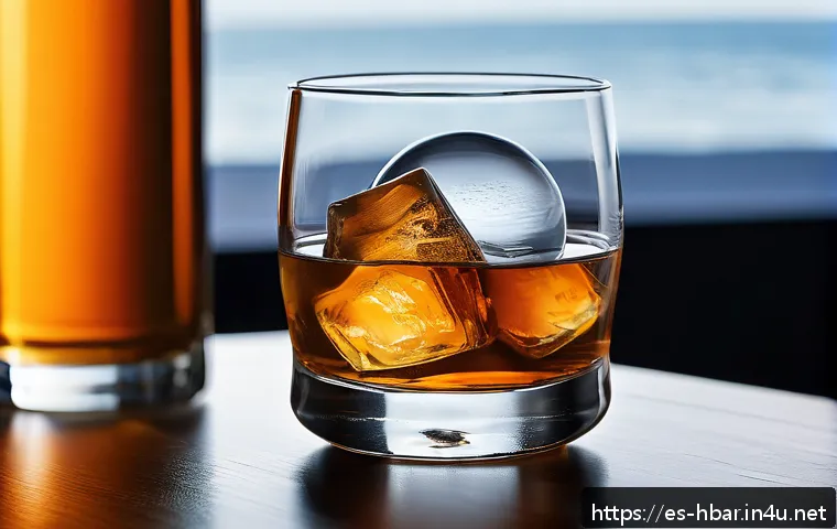 홈바텐더 얼음 종류 및 사용법 - A close-up of a sophisticated cocktail glass filled with a premium whisky on the rocks, featuring a ...